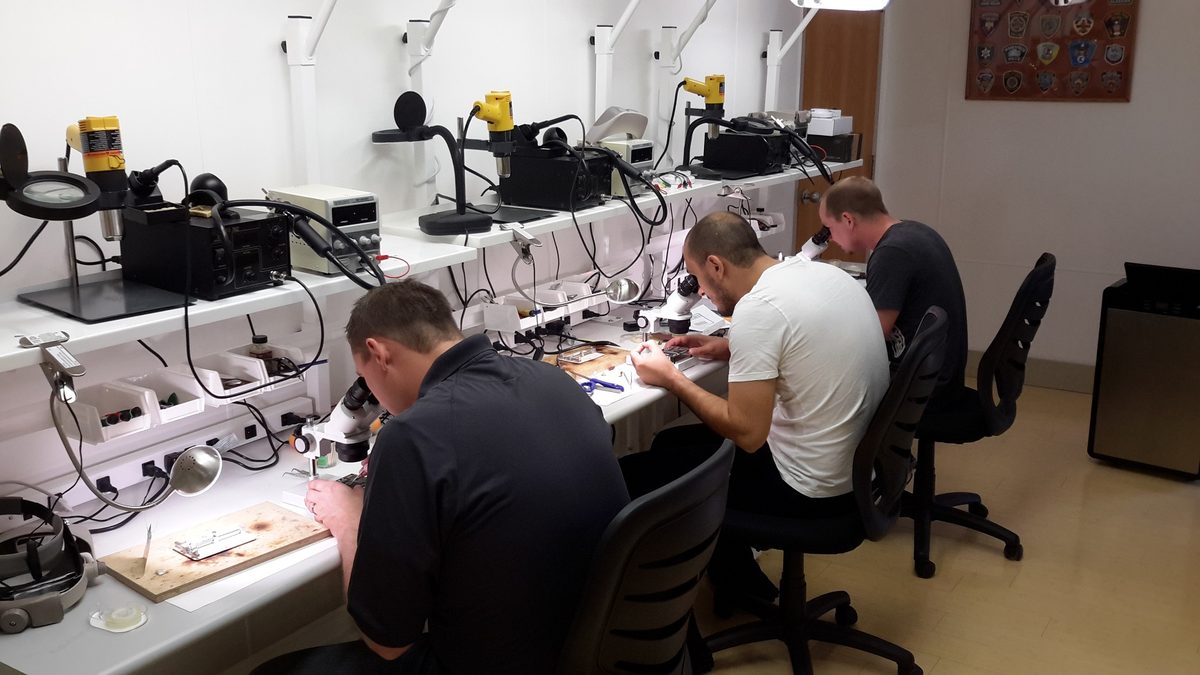 Deux techniciens du laboratoire travaillant au microscope binoculaire sur des cartes électroniques de disques durs.
